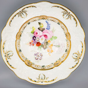 A finely painted Swansea porcelain dish, with ‘C scroll’ embossed borders within a gilt rim, the centre with garden flowers within a complex gilt border. About 1815-17 Diameter 21.5cm Painted red SWANSEA uppercase mark to base